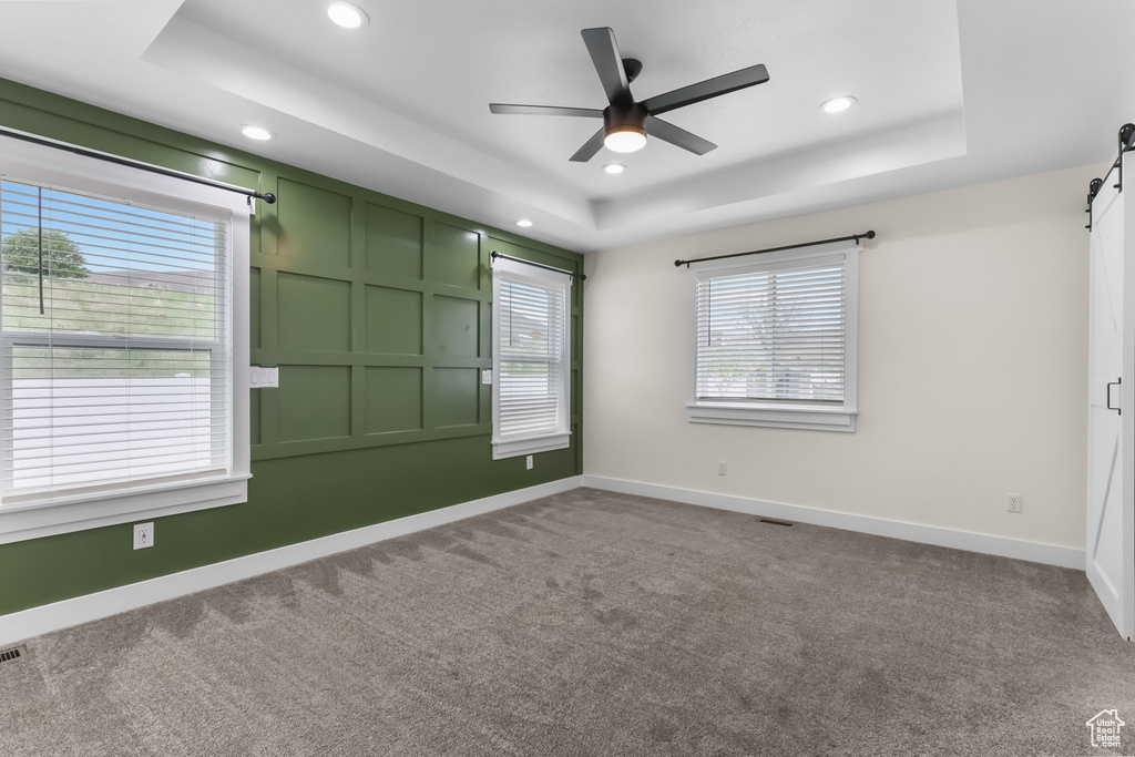 Spare room with a raised ceiling, a barn door, recessed lighting, ceiling fan, and carpet