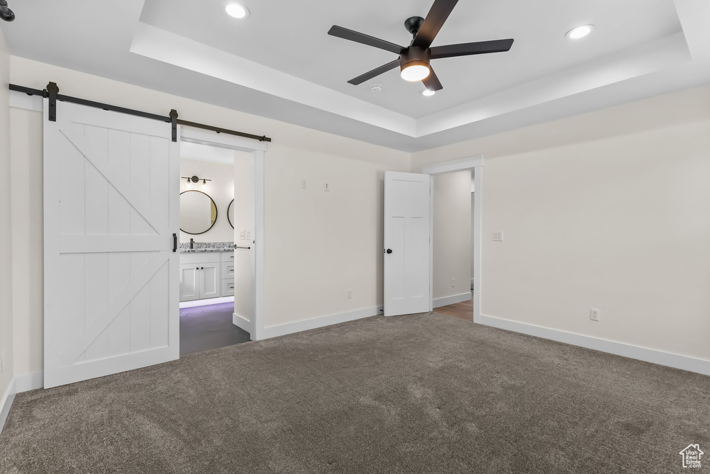 Unfurnished bedroom featuring a tray ceiling, dark carpet, a barn door, recessed lighting, and baseboards