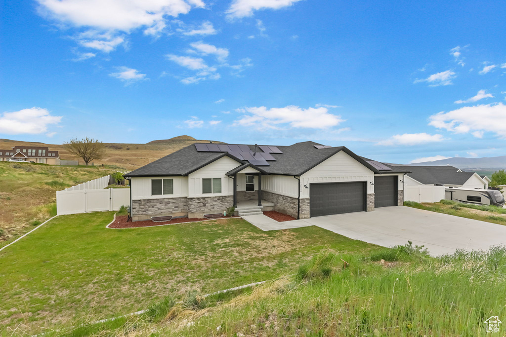 View of front of property featuring a garage, a gate, driveway, roof mounted solar panels, and stone siding