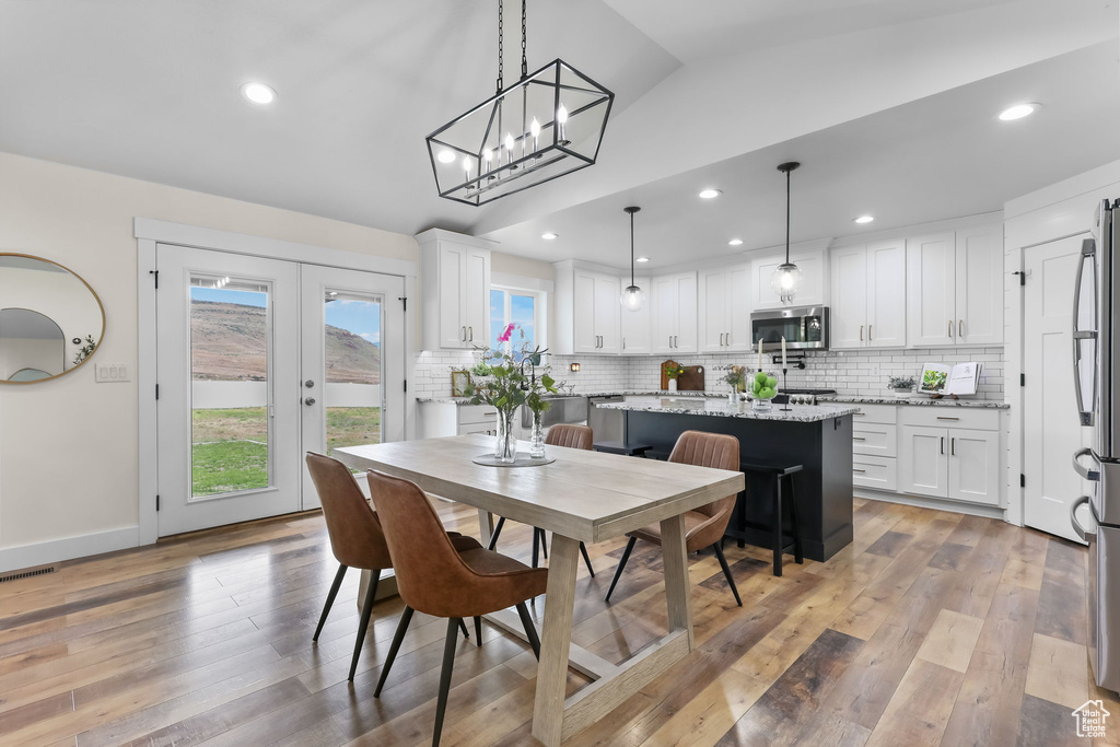 Dining area with vaulted ceiling, light wood-type flooring, recessed lighting, a chandelier, and french doors