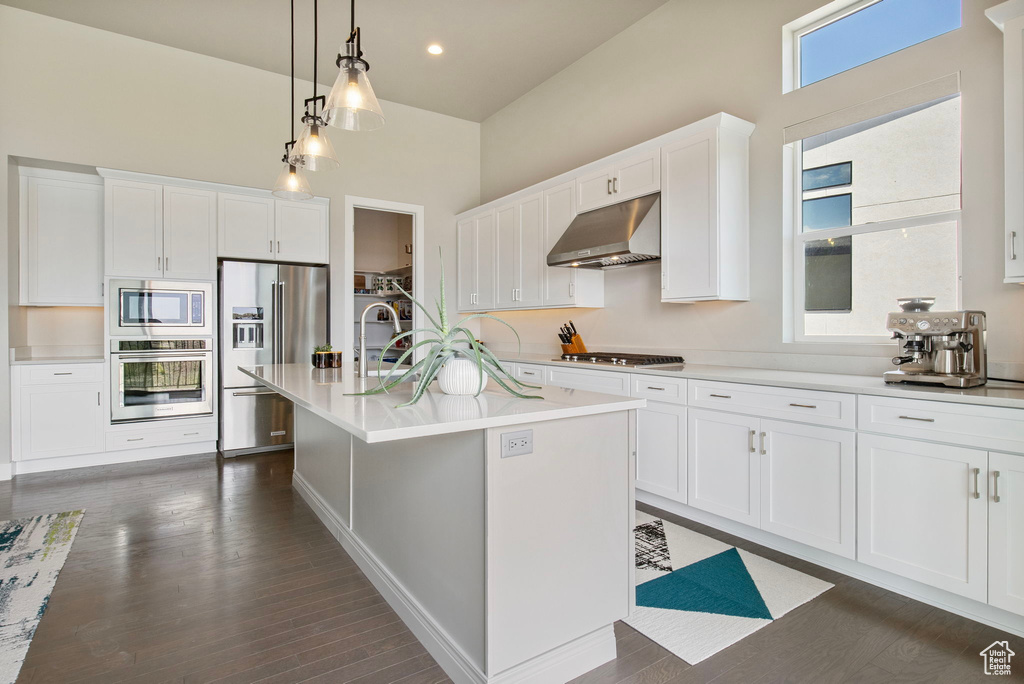 Kitchen with under cabinet range hood, stainless steel appliances, white cabinets, light countertops, and a high ceiling