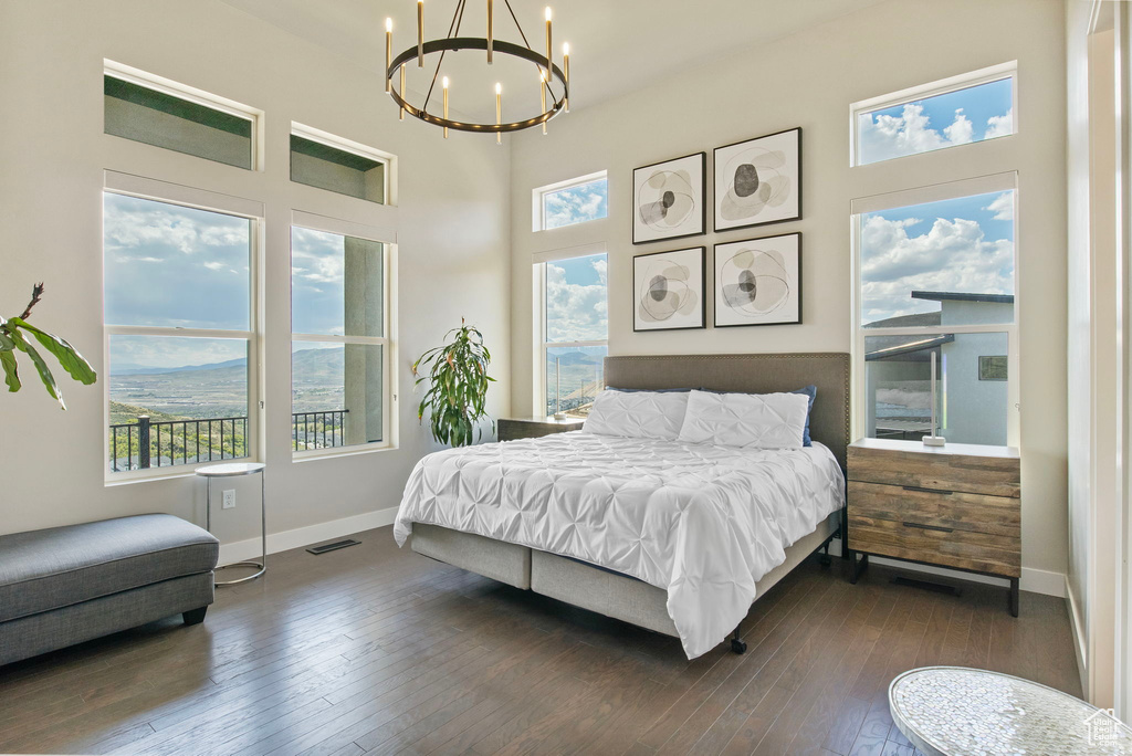 Bedroom with a chandelier, multiple windows, dark wood finished floors, baseboards, and a high ceiling