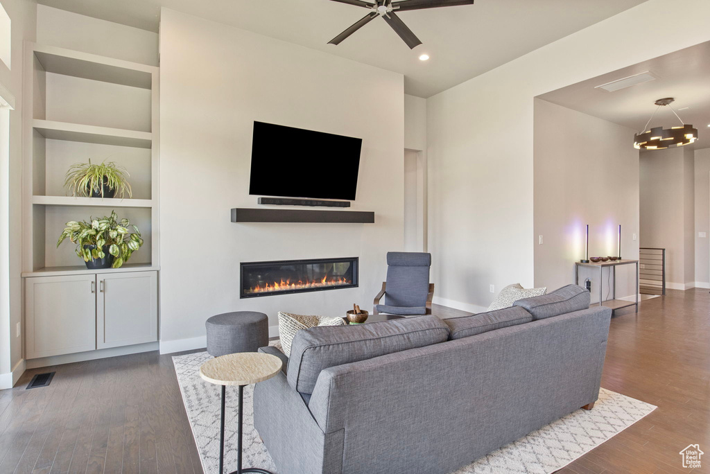 Living area with a glass covered fireplace, wood finished floors, baseboards, built in features, and ceiling fan
