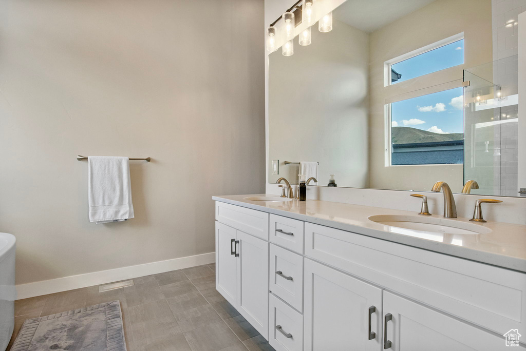 Full bath with double vanity, tiled shower, and baseboards