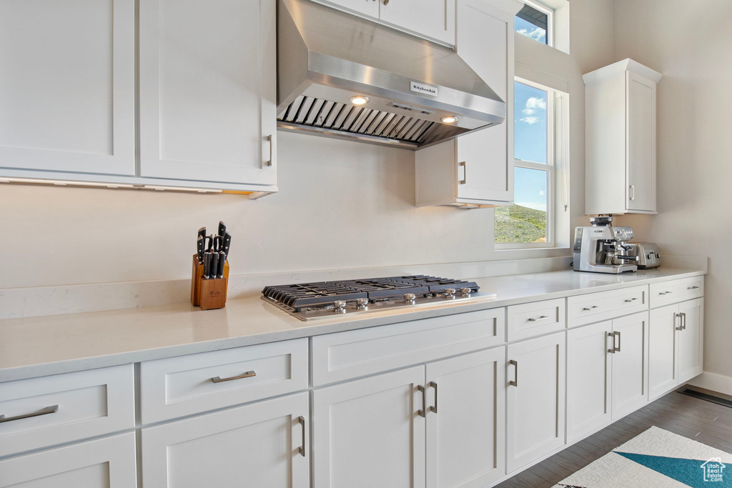 Kitchen featuring range hood, stainless steel gas cooktop, white cabinetry, and light countertops
