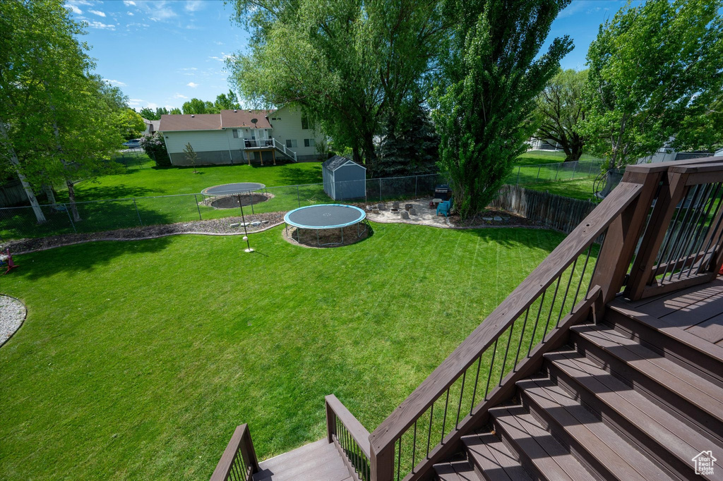 View of yard featuring a wooden deck, a storage shed, an outdoor structure, and a trampoline