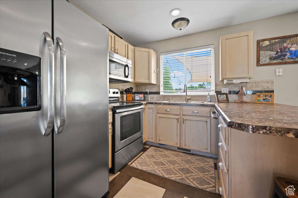 Kitchen featuring appliances with stainless steel finishes, a sink, dark countertops, tasteful backsplash, and dark wood finished floors