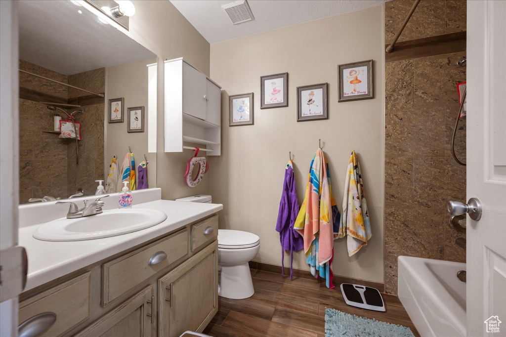 Full bath featuring wood finished floors, toilet, vanity, shower / bath combination, and baseboards