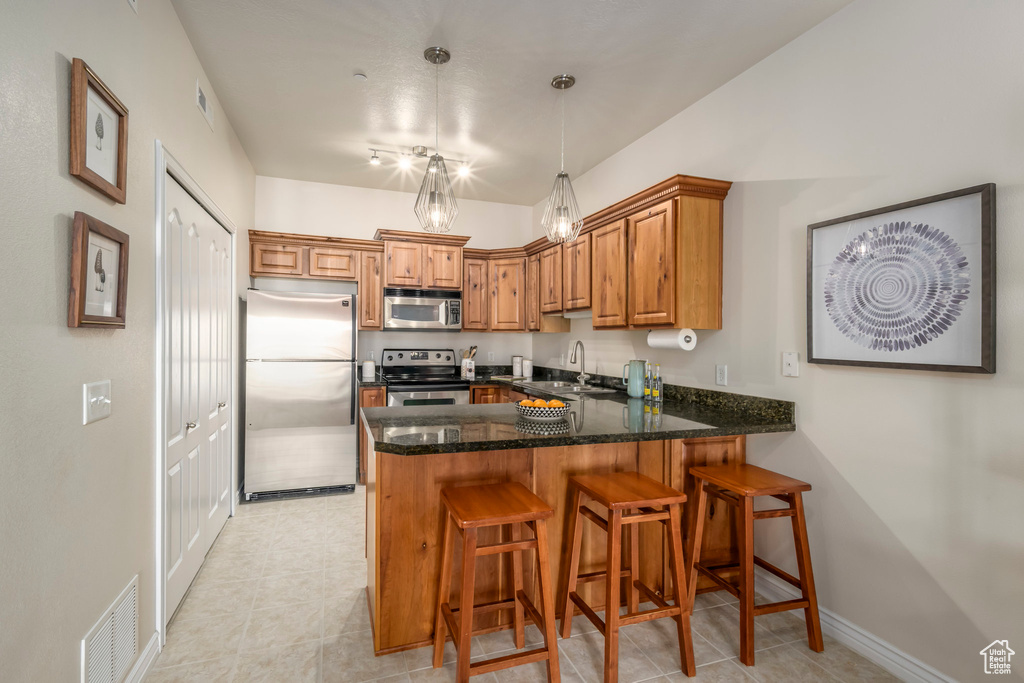 Kitchen featuring appliances with stainless steel finishes, a peninsula, a sink, brown cabinetry, and dark stone countertops