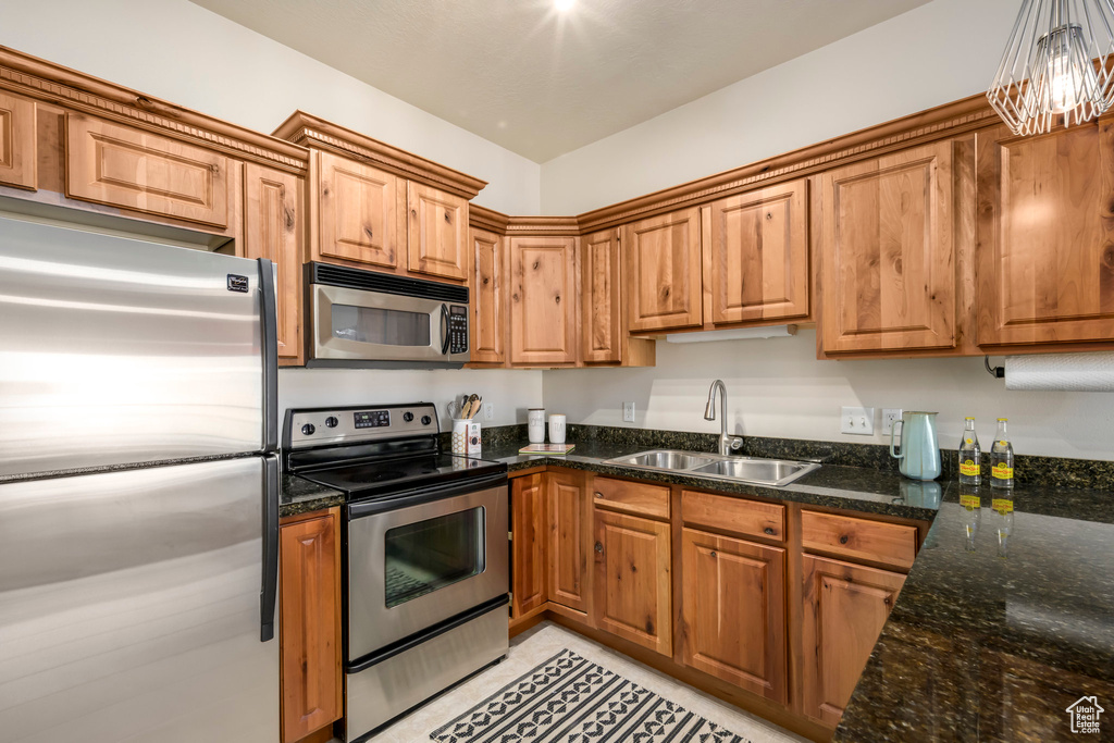 Kitchen featuring appliances with stainless steel finishes, a sink, brown cabinets, and dark stone counters