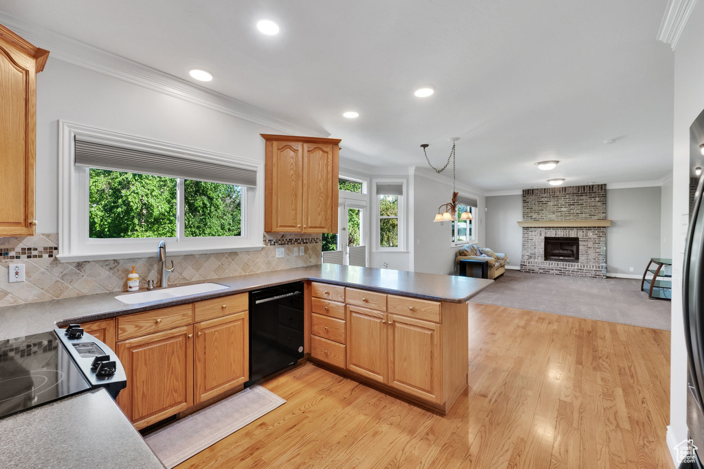 Kitchen with black dishwasher, a sink, ornamental molding, a brick fireplace, and light wood finished floors