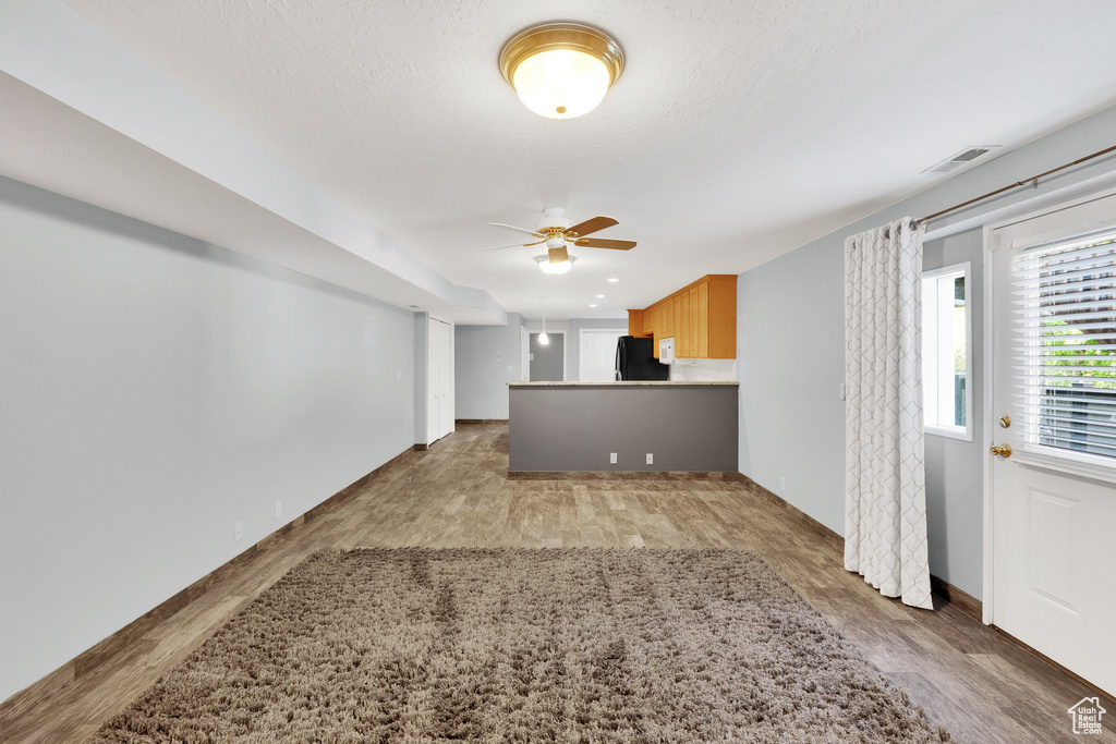 Unfurnished living room featuring wood finished floors, a ceiling fan, and baseboards
