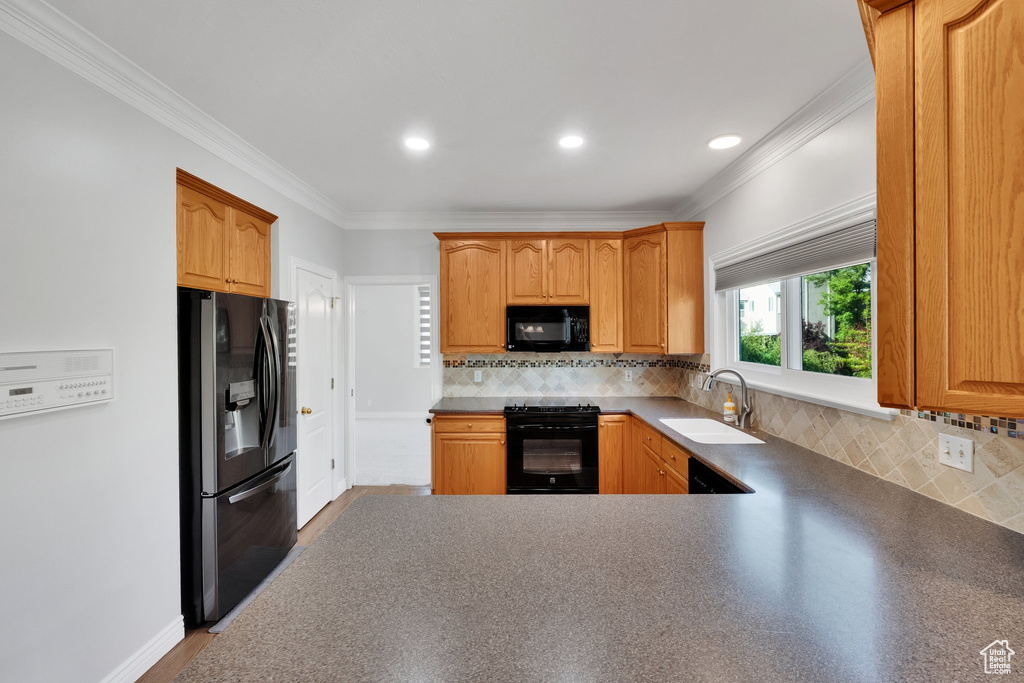 Kitchen featuring black appliances, a sink, ornamental molding, decorative backsplash, and dark countertops