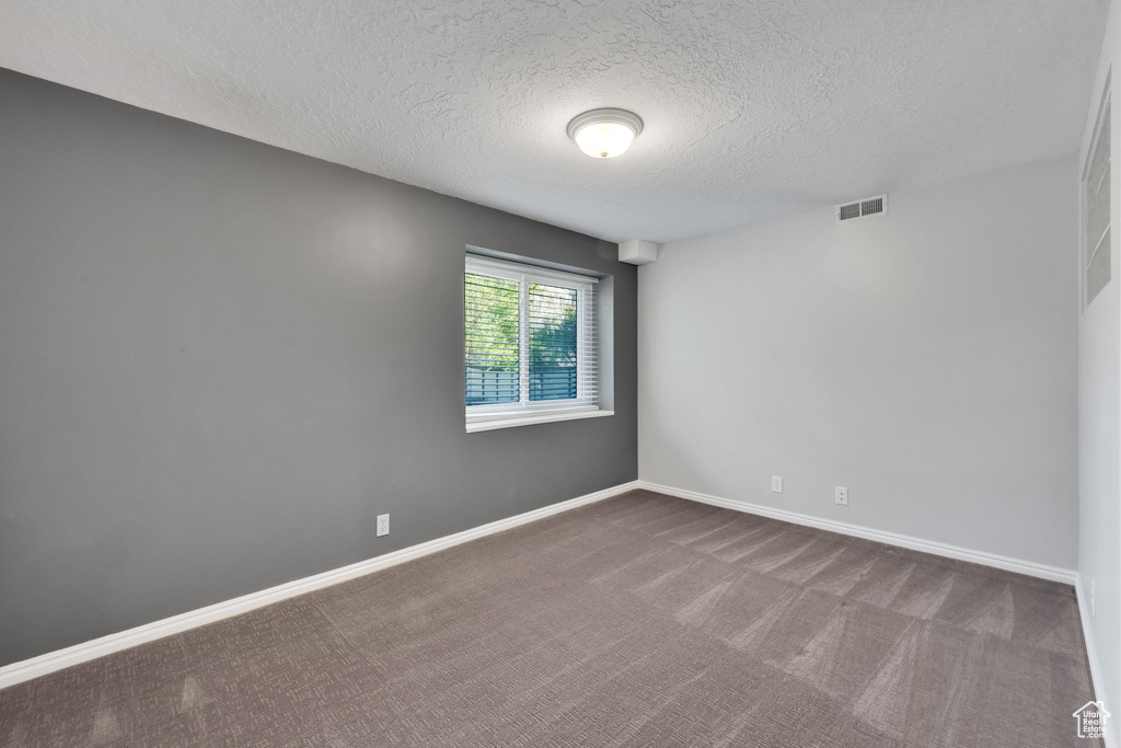 Spare room with a textured ceiling, dark colored carpet, and baseboards