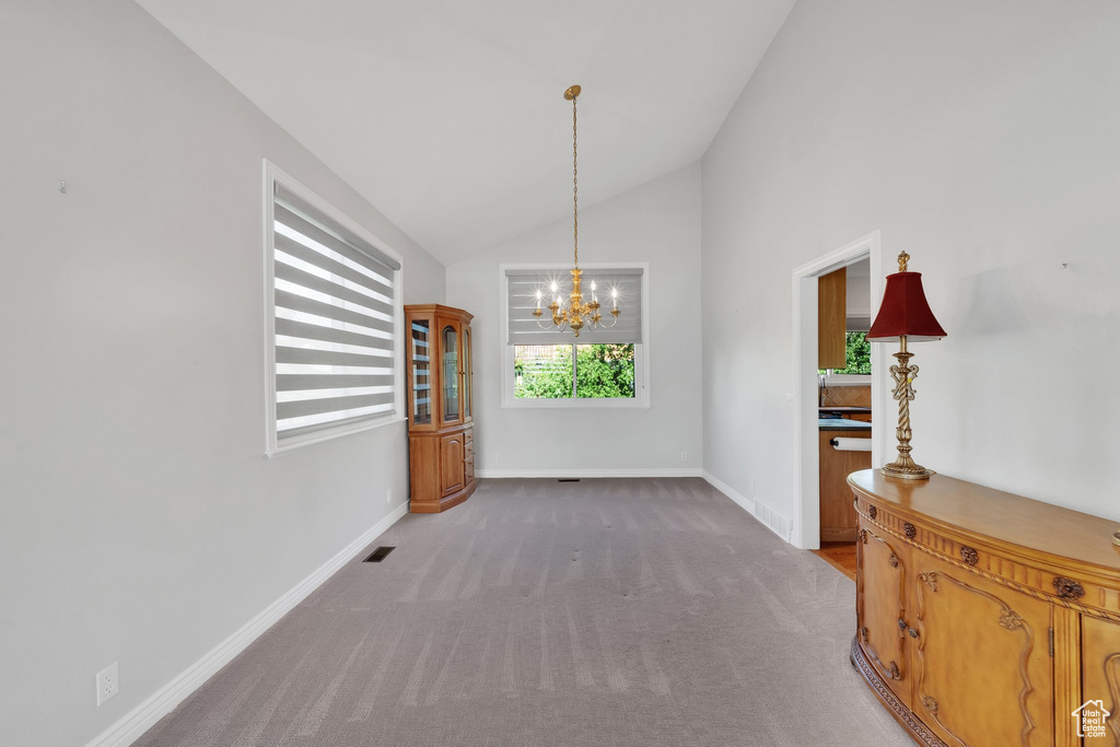 Unfurnished dining area featuring a chandelier, lofted ceiling, plenty of natural light, carpet flooring, and baseboards