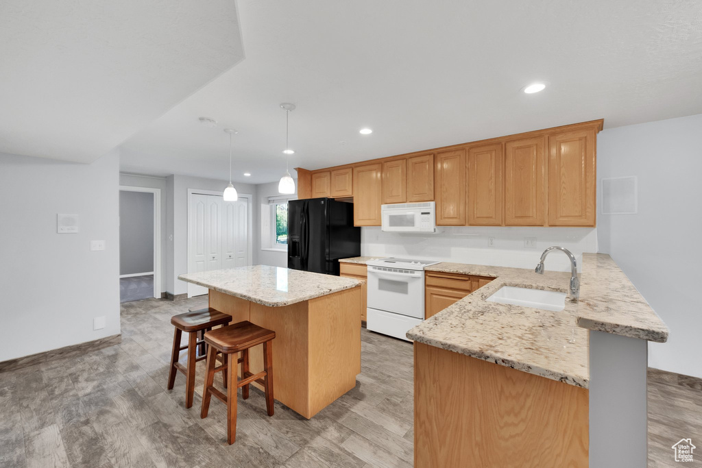 Kitchen featuring white appliances, a sink, a breakfast bar, light wood-type flooring, and recessed lighting