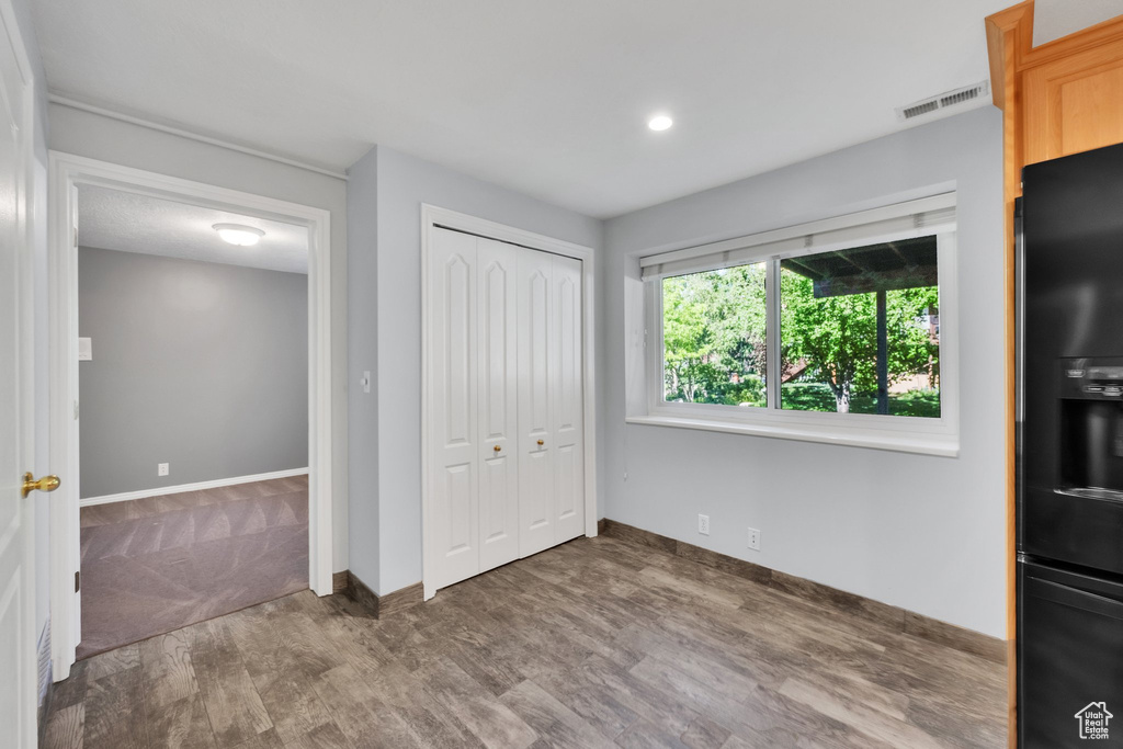 Unfurnished bedroom with black refrigerator with ice dispenser, wood finished floors, baseboards, a closet, and recessed lighting
