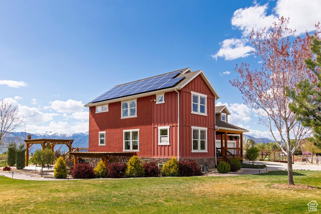 View of side of property with roof mounted solar panels, board and batten siding, a pergola, and a yard