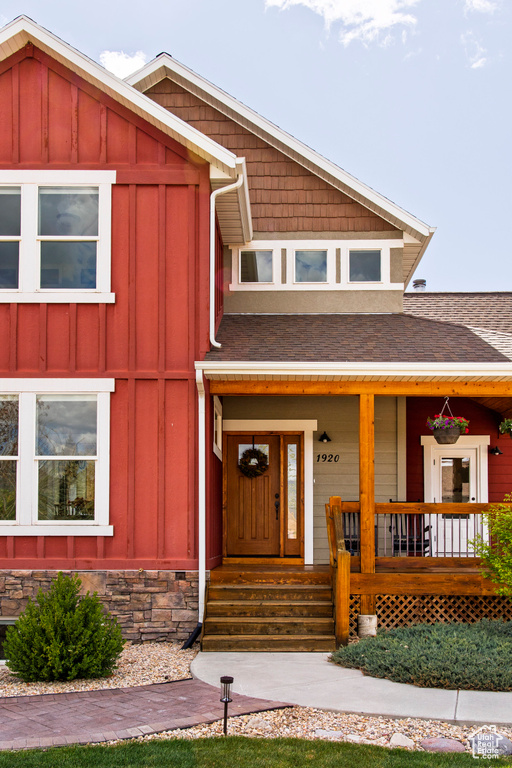 View of front of house with board and batten siding, roof with shingles, and covered porch