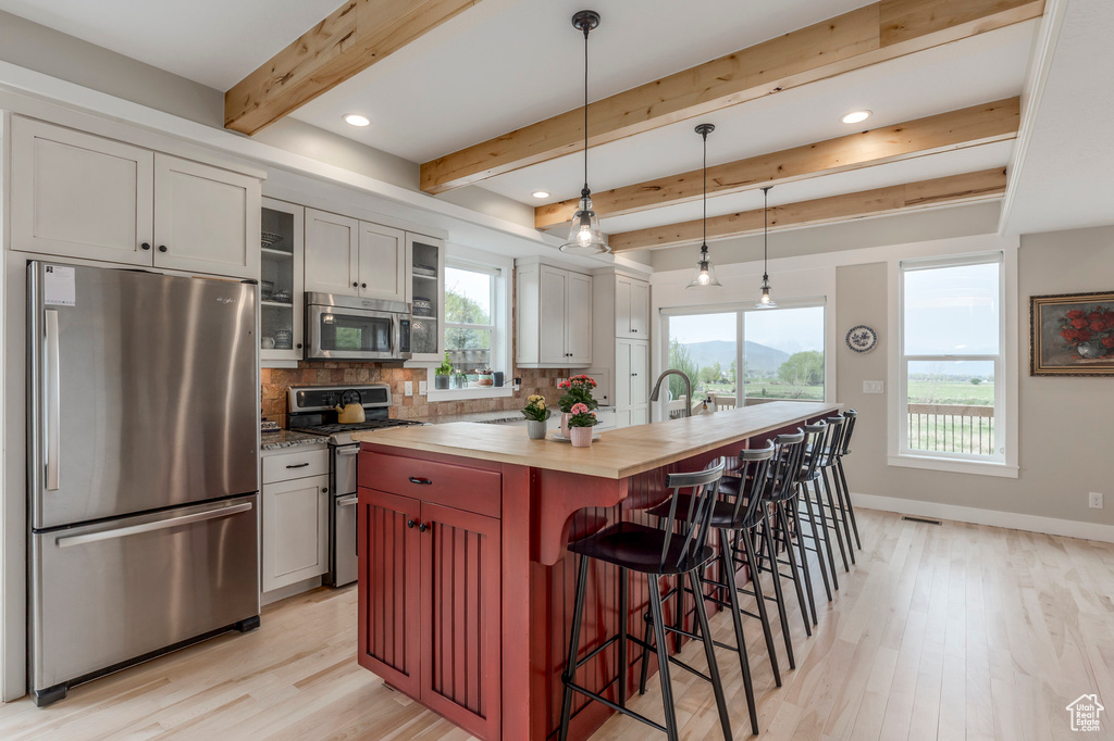 Kitchen featuring appliances with stainless steel finishes, wood counters, light wood-style floors, tasteful backsplash, and beam ceiling