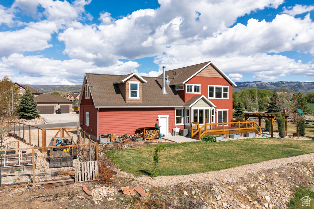 Back of property featuring a deck with mountain view, roof with shingles, and a gate