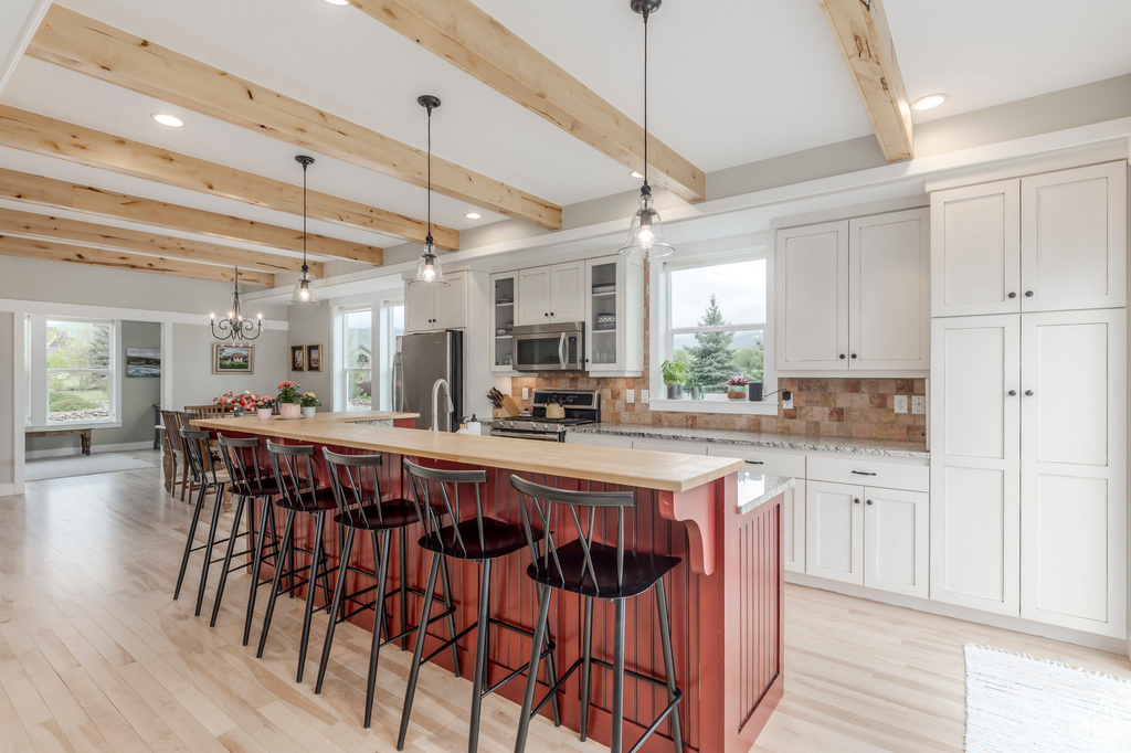 Kitchen featuring appliances with stainless steel finishes, light wood-type flooring, a large island, decorative backsplash, and beamed ceiling