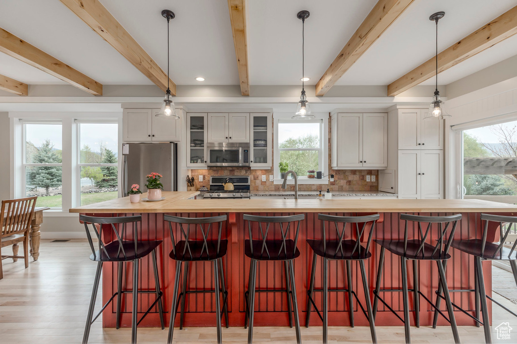 Kitchen with stainless steel appliances, backsplash, butcher block countertops, glass insert cabinets, and white cabinets
