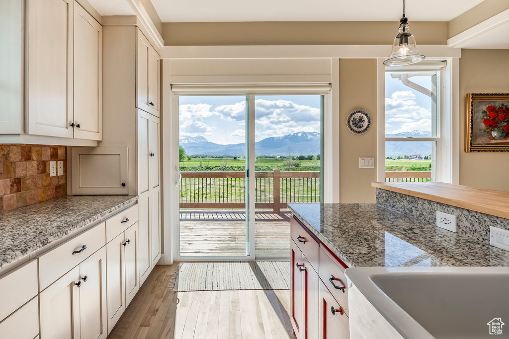 Kitchen featuring a mountain view, light wood-type flooring, decorative backsplash, hanging light fixtures, and light stone counters