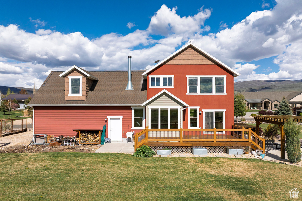 Back of house with a wooden deck, a lawn, roof with shingles, and a patio