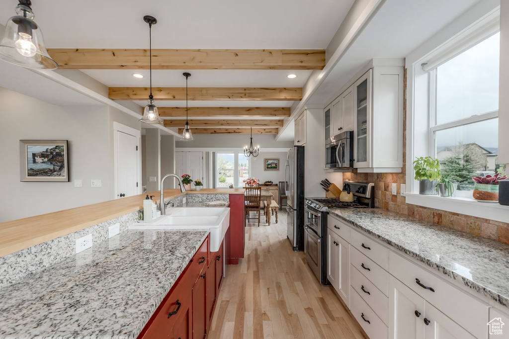 Kitchen with appliances with stainless steel finishes, a chandelier, light wood finished floors, beamed ceiling, and backsplash