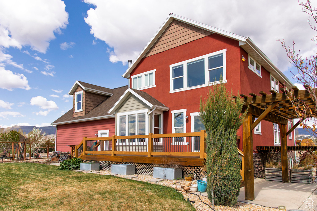 Rear view of house featuring a deck with mountain view, a pergola, a lawn, and roof with shingles