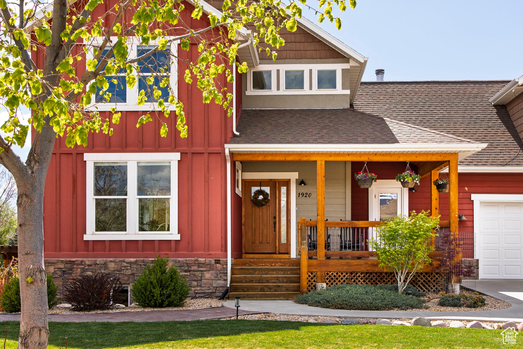 View of front facade featuring board and batten siding, roof with shingles, covered porch, and an attached garage