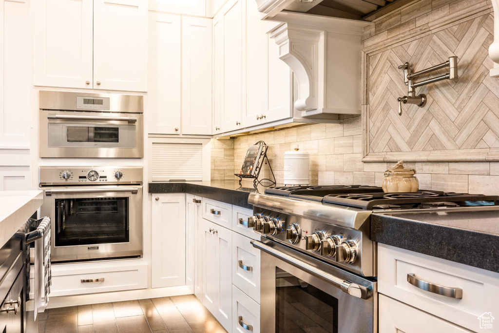 Kitchen with appliances with stainless steel finishes, dark countertops, tasteful backsplash, and white cabinets