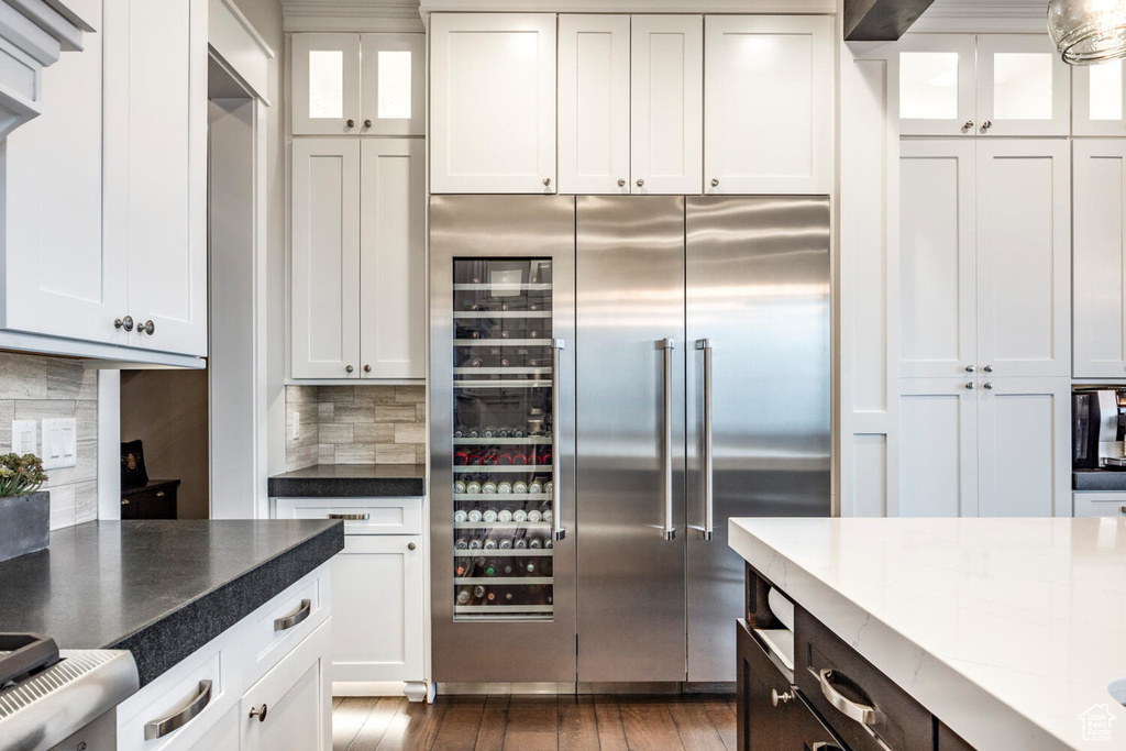 Kitchen with built in fridge, glass insert cabinets, tasteful backsplash, and white cabinetry