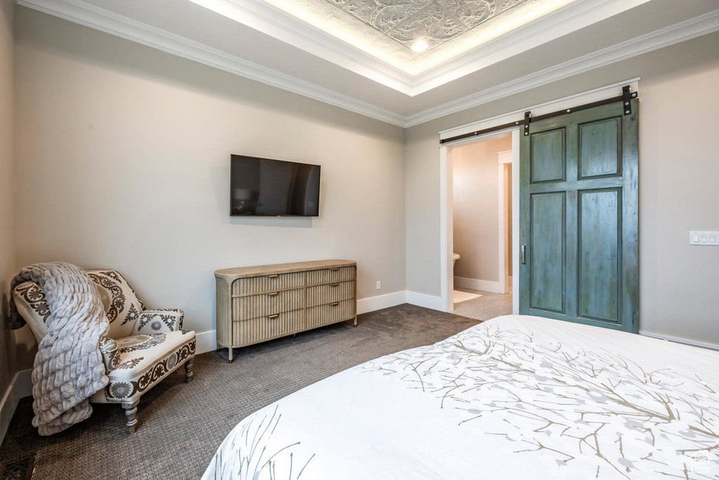 Bedroom featuring carpet, a barn door, a raised ceiling, ornamental molding, and baseboards