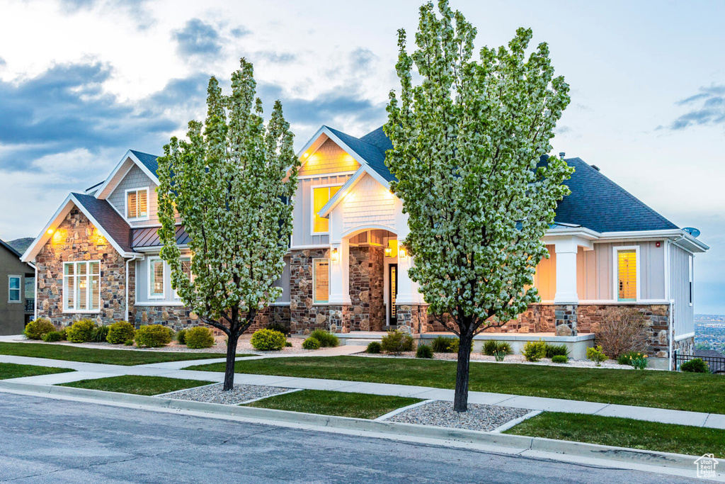 Craftsman inspired home featuring stone siding, a front yard, board and batten siding, a standing seam roof, and roof with shingles