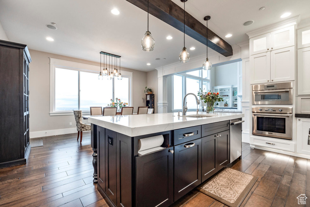 Kitchen with dark wood finished floors, appliances with stainless steel finishes, white cabinetry, a sink, and pendant lighting