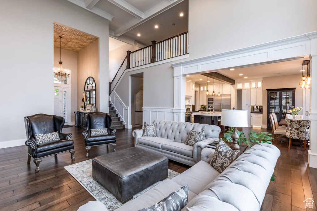 Living room featuring a chandelier, a towering ceiling, dark wood-type flooring, stairs, and recessed lighting