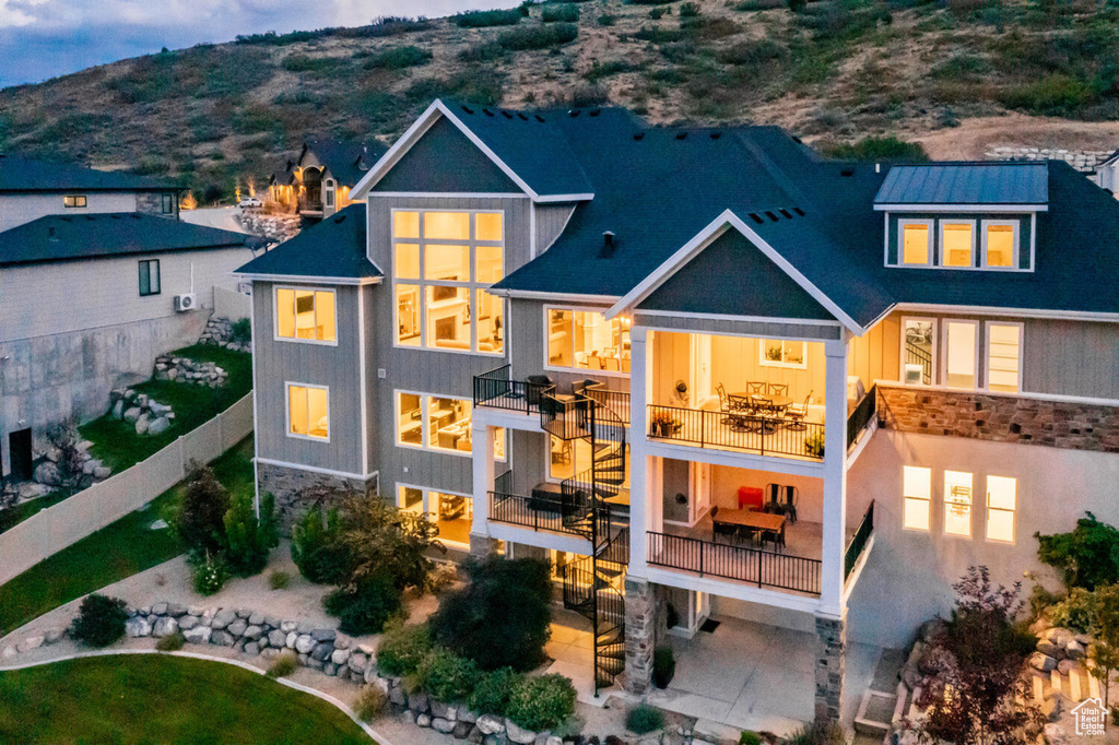 Back of house with a balcony, stone siding, fence, a mountain view, and a patio