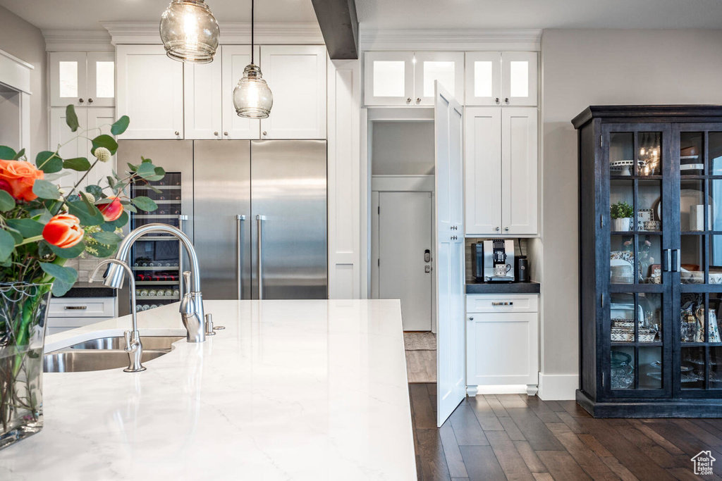 Kitchen with built in fridge, a sink, dark wood finished floors, white cabinetry, and hanging light fixtures