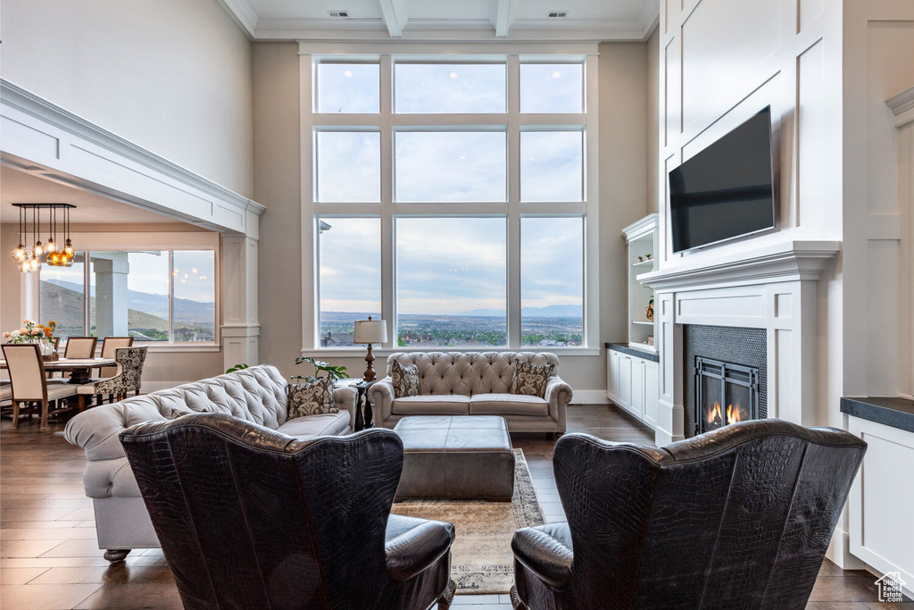 Living room with a high ceiling, a glass covered fireplace, beam ceiling, a chandelier, and dark wood-style floors