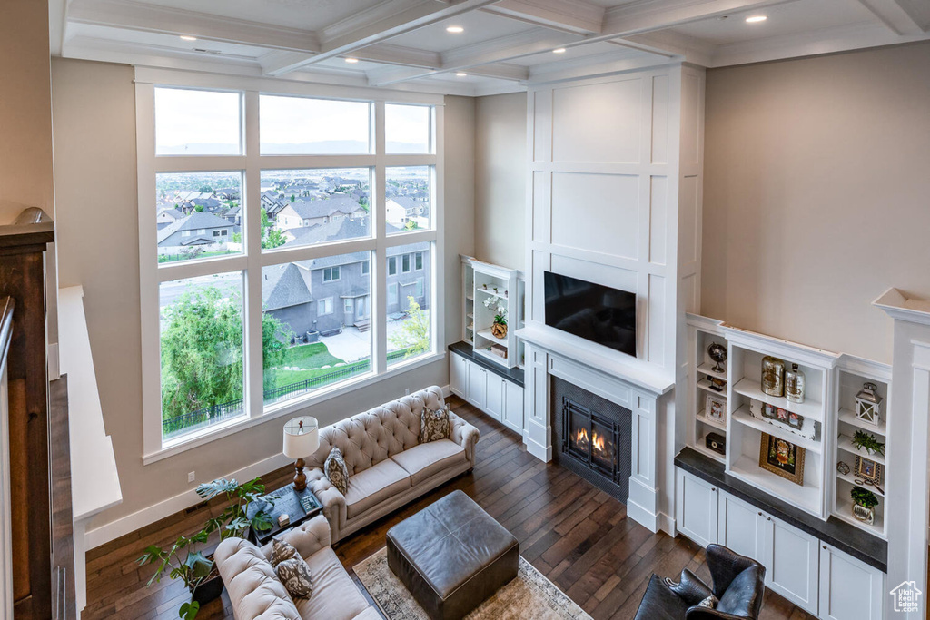 Living area with a glass covered fireplace, dark wood finished floors, beam ceiling, healthy amount of natural light, and coffered ceiling