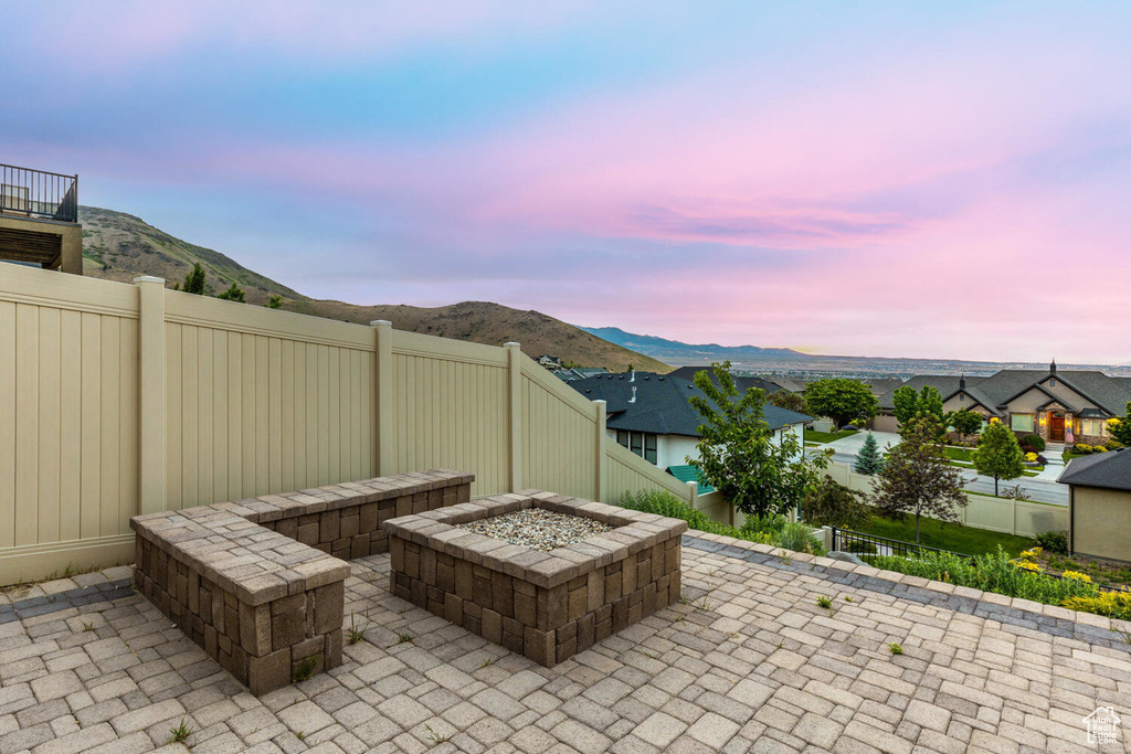 Patio terrace at dusk with an outdoor fire pit, a fenced backyard, and a mountain view