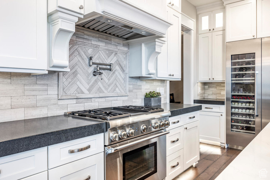 Kitchen featuring high quality appliances, premium range hood, white cabinetry, dark countertops, and decorative backsplash