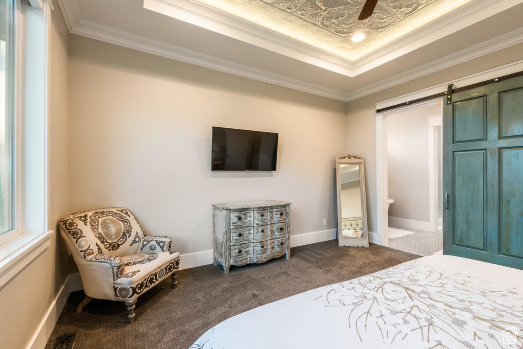 Bedroom with dark colored carpet, a raised ceiling, crown molding, a barn door, and baseboards