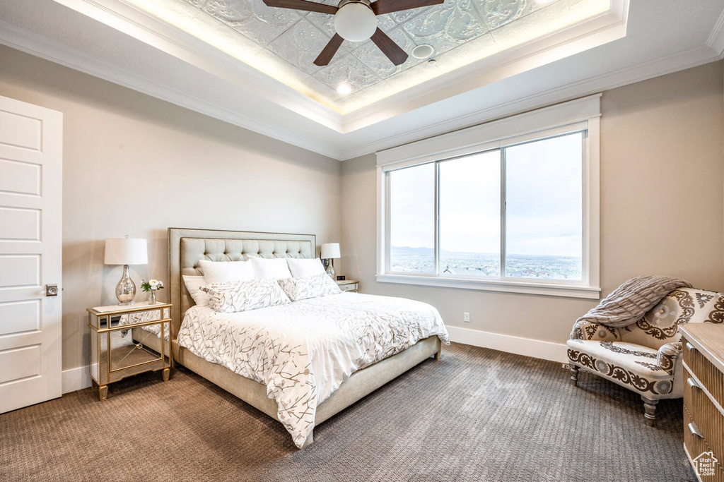 Carpeted bedroom featuring a raised ceiling, baseboards, ornamental molding, and ceiling fan