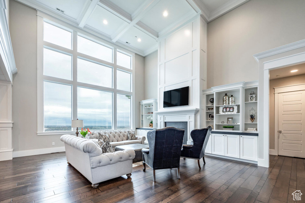 Living area with a high ceiling, healthy amount of natural light, a fireplace, ornamental molding, and dark wood-style flooring