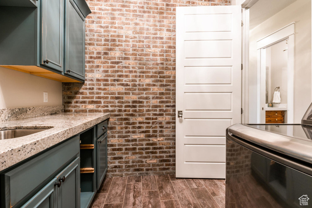 Kitchen with brick wall, light stone counters, dark wood-type flooring, and stove
