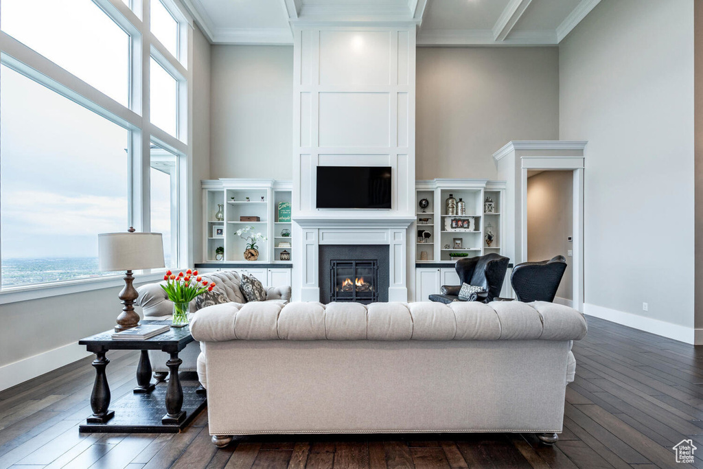 Living room with healthy amount of natural light, a warm lit fireplace, baseboards, ornamental molding, and a towering ceiling
