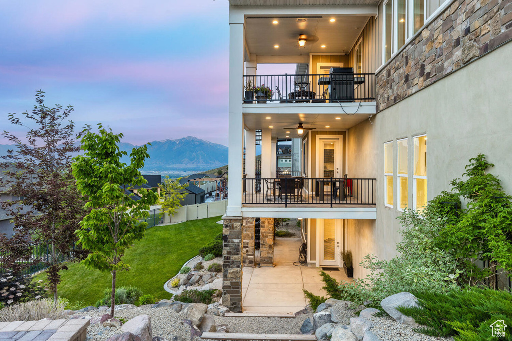 Back of property at dusk with a balcony, a patio area, stucco siding, and a mountain view